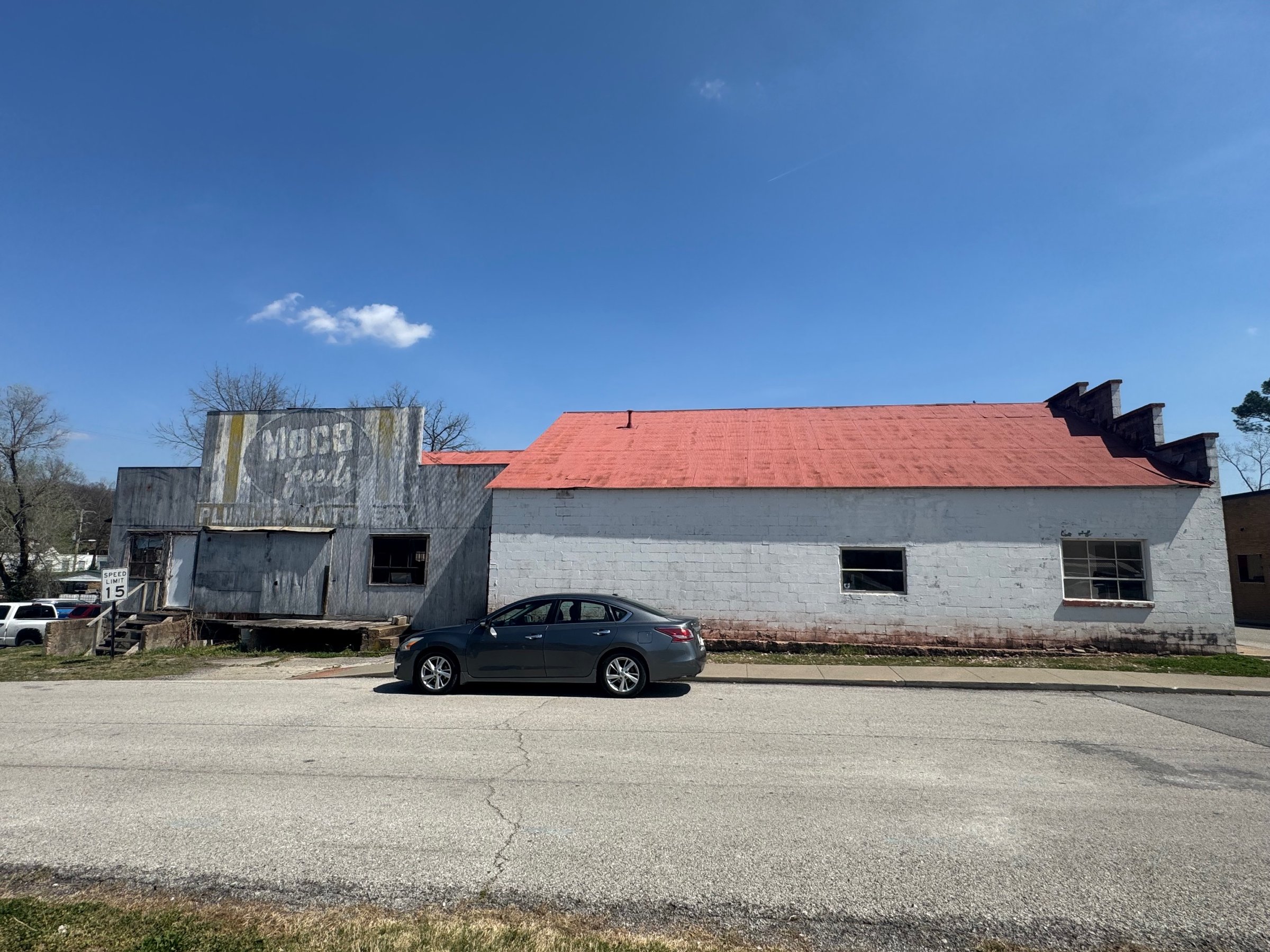 The side of the Riverbend Hollow building today: a white block wall with a red metal roof beside a weathered wooden facade with a faded painted sign