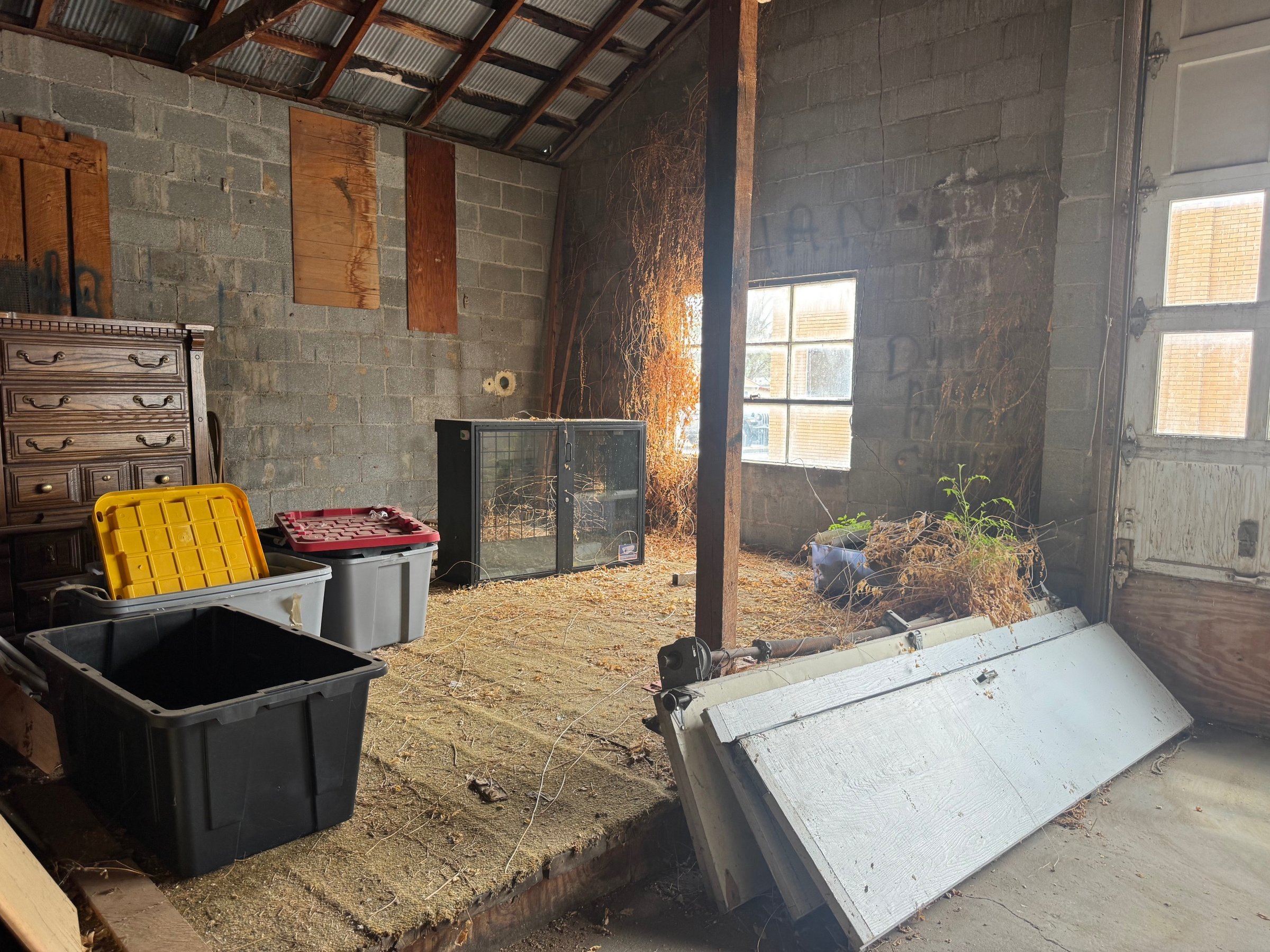 The building's interior today: bare block walls, exposed rafters and tin roof, with stored bins and furniture awaiting renovation